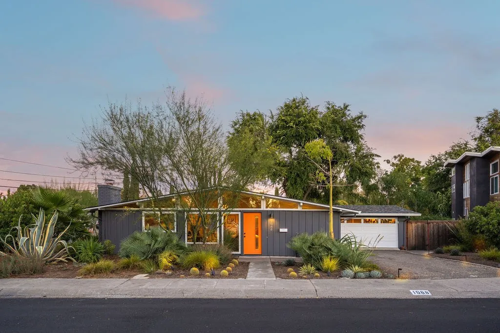 Twilight photo of a mid-century home with an orange front door